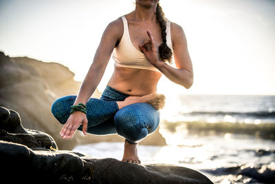 Low section of woman exercising on rock against sea