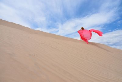 Mid adult woman with coral dupatta at desert against sky