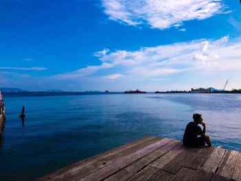 Rear view of woman sitting on pier over sea against sky