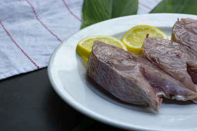 Fresh raw fish on white plate with green leaf and lemon