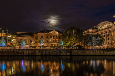 Illuminated buildings by river at night