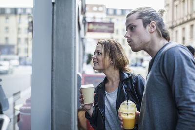 Couple holding disposable cups while window shopping