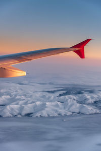 Airplane flying over snowcapped mountains against sky during sunset