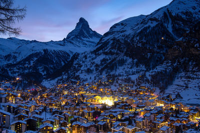 Buildings by snowcapped mountain in town at dusk