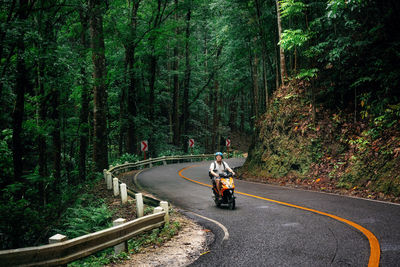 Rear view of people riding bicycle on road in forest