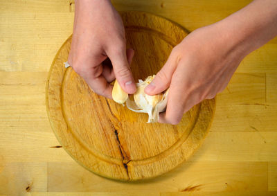 Cropped hands breaking garlic clove over cutting board