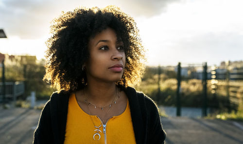 Close-up of thoughtful beautiful woman with afro hair against sky