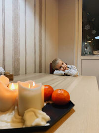 The boy put his head on the table. candles and fruits in the foreground