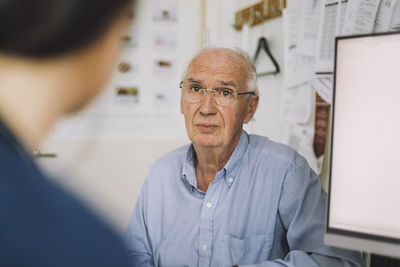 Senior male patient wearing eyeglasses and listening to nurse during visit in clinic