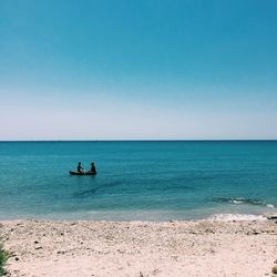 People on boat in blue sea against clear sky on sunny day