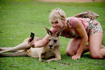 Happy woman taking selfie with kangaroo on grassy field