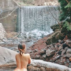 Rear view of shirtless man looking at waterfall