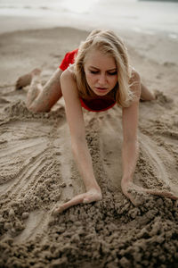 A girl in a red dress draws on the white sea sand