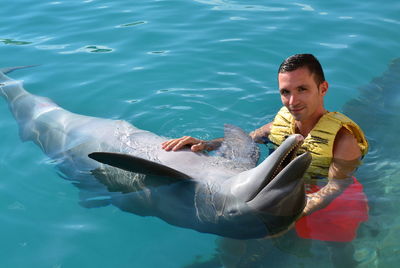 High angle portrait of young man holding dolphin in sea