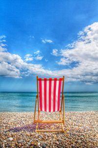 Empty folded chair on beach against sky