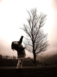 Woman standing by bare tree on field against sky