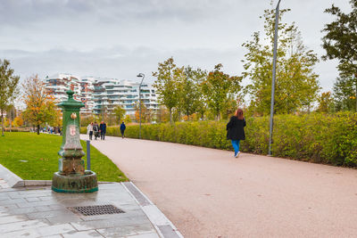 Rear view of woman walking on footpath in city against sky