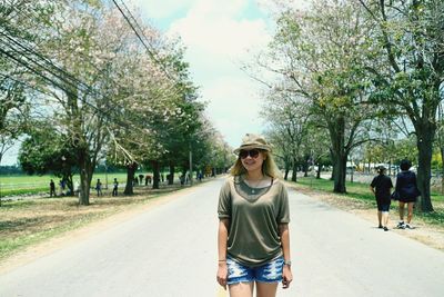 Portrait of smiling woman standing on road against trees