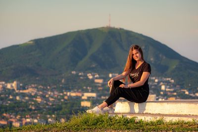 Portrait of woman sitting on mountain against sky