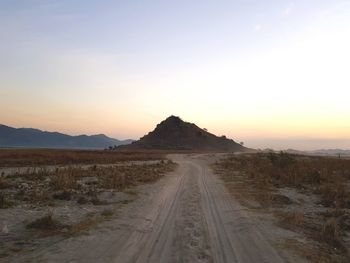 Dirt road amidst land against sky during sunset