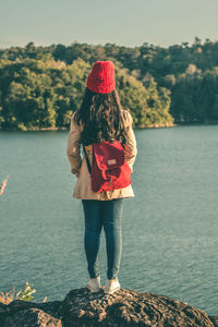 Rear view full length of woman standing by lake on rock