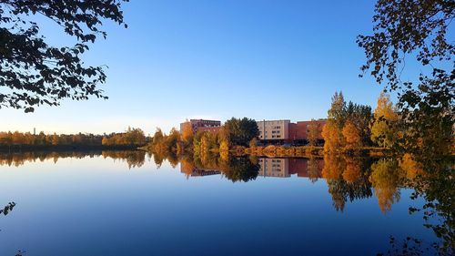 Reflection of trees and buildings in lake against clear blue sky