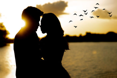 Silhouette woman with birds against sky during sunset