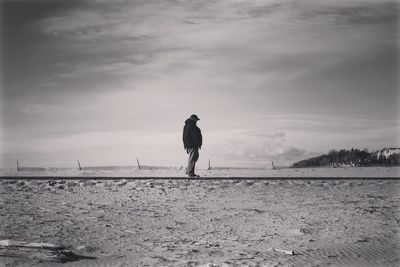 Man standing at beach against cloudy sky