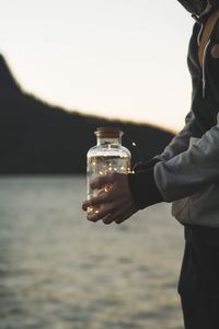 Close-up of man holding drink against sea