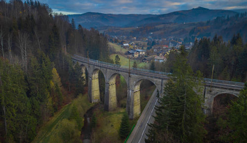 Arch bridge amidst trees and mountains against sky