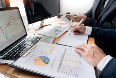 Midsection of businessmen discussing paperwork on desk