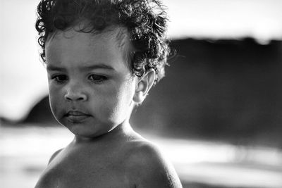 Close-up of shirtless boy looking down at beach