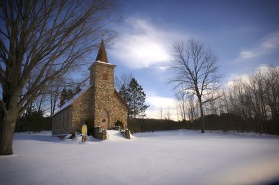 Low angle view of church on snowy field amidst trees against sky