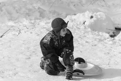 Boy with sled crouching on snowy field