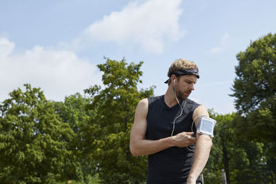 Man listening music while exercising against trees