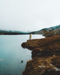 Man standing on rock by lake against sky