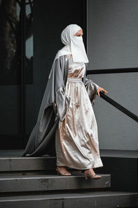 Full length image of veiled woman with white niqab walking down the stairs