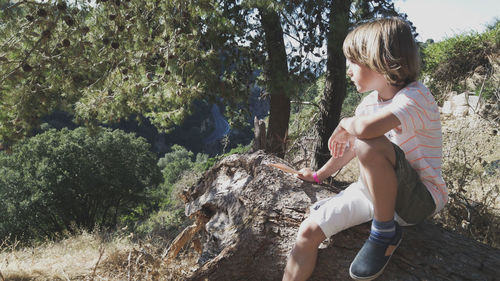 Side view of boy sitting on tree trunk