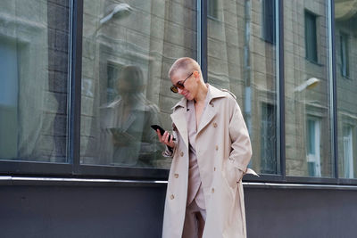 Smiling businesswoman using mobile while standing against building