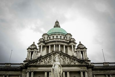 Low angle view of statue and belfast city hall against cloudy sky