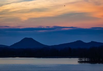 Scenic view of lake by silhouette mountains against sky