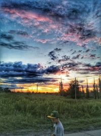 Rear view of man standing on field against dramatic sky