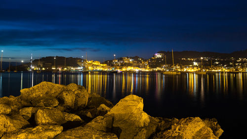 Illuminated city by sea against sky at night