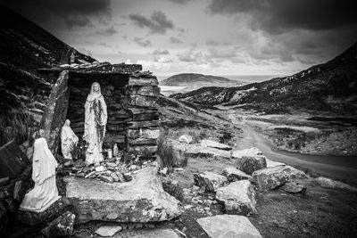 Virgin mary statue on rocks at field against sky