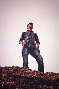 Young man standing on rock against sky