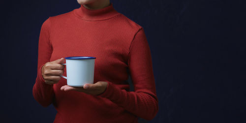 Midsection of man holding coffee cup against black background