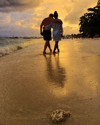 Men on beach against sky during sunset
