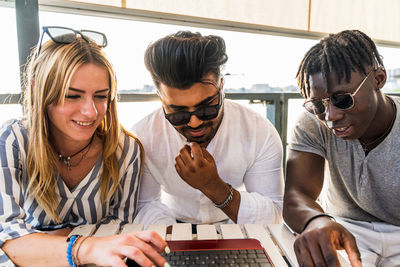 Small group of multiethnic friends having fun surfing the net on a laptop - summer vacation concept