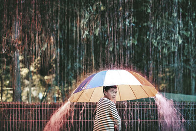 Portrait of boy holding umbrella during rainy season