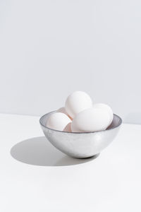 Bowl with fresh chicken eggs placed on table on white background in studio